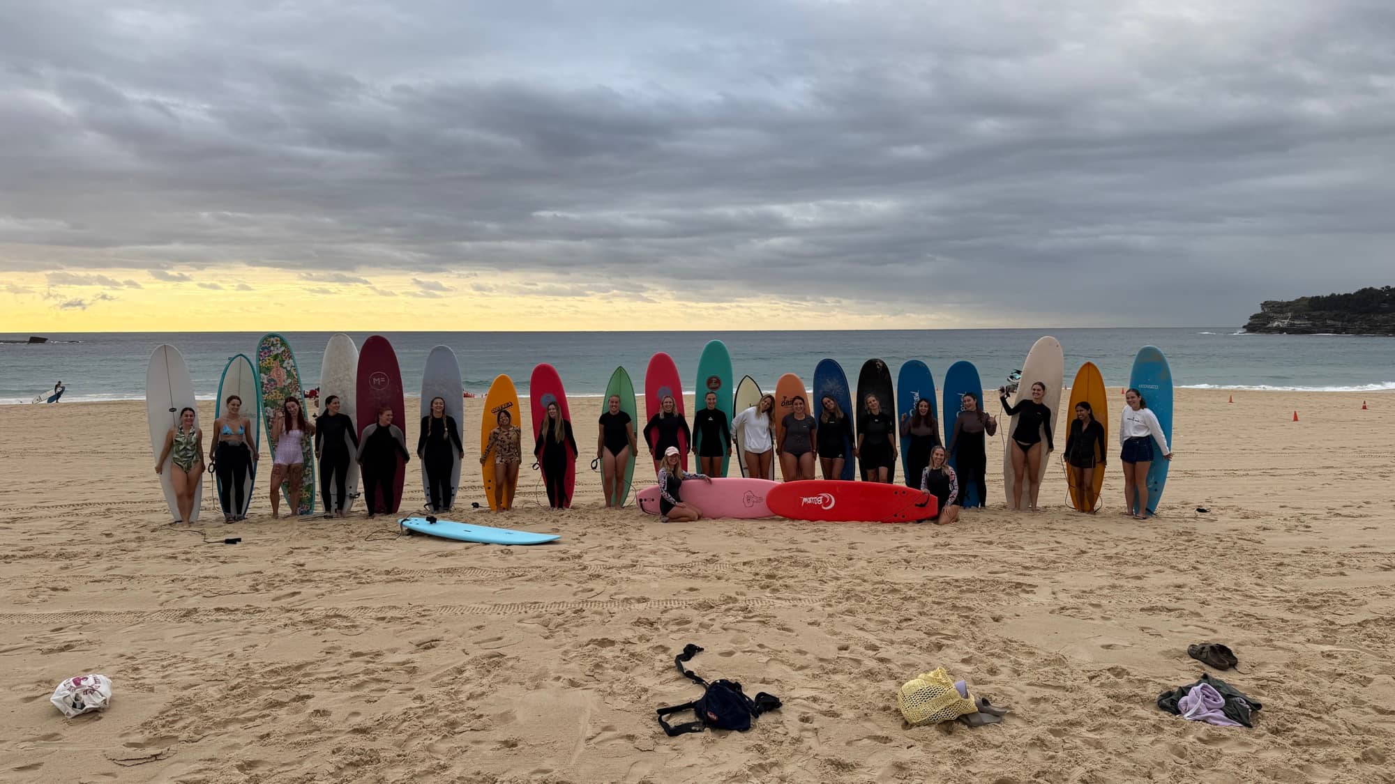 Women from the Bondi Surf Sisters community lined up on the sand with colourful softboards at Bondi Beach